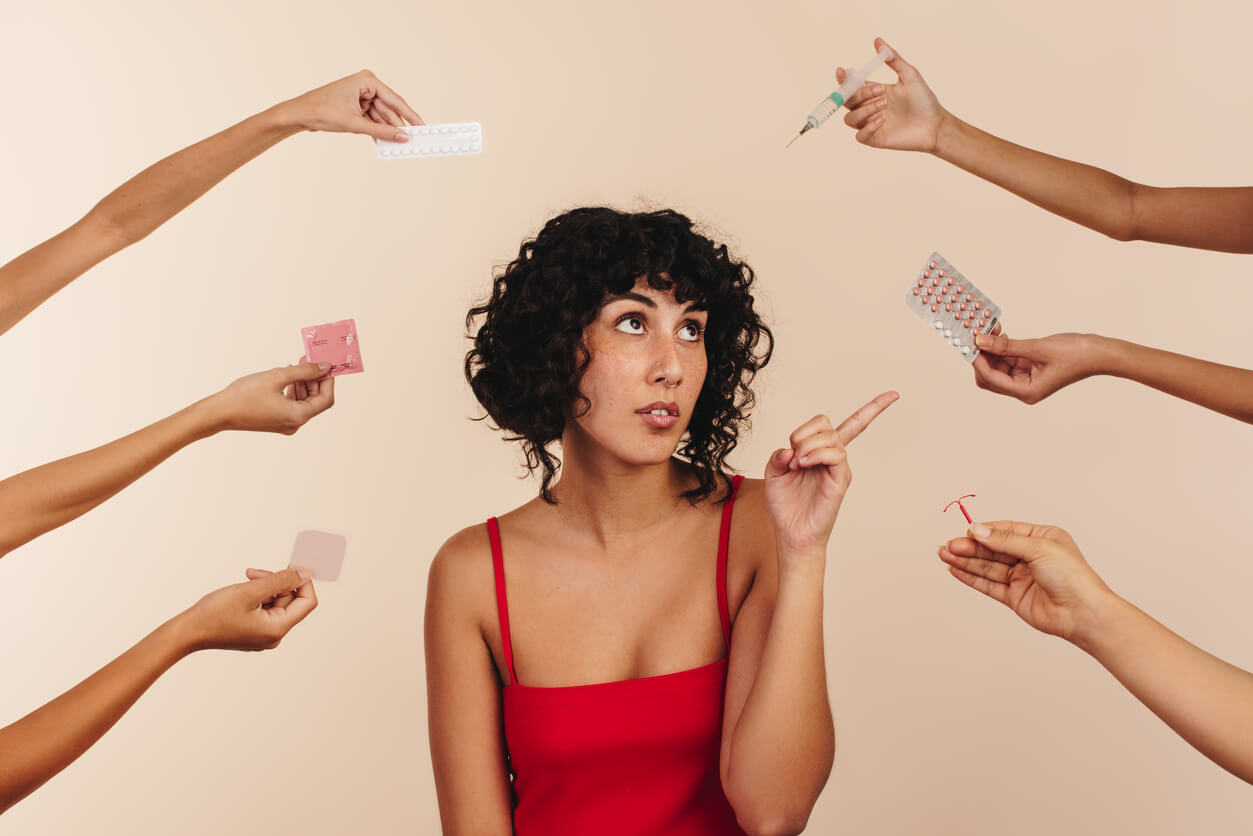 young woman pointing at birth control while surrounded by hands holding different forms of hormonal and non-hormonal contraception.
