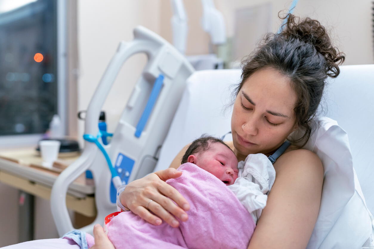A beautiful and relaxed ethnic mother is snuggling her newborn and affectionately holding her in the hospital after delivery. Skin to skin bonding concept.