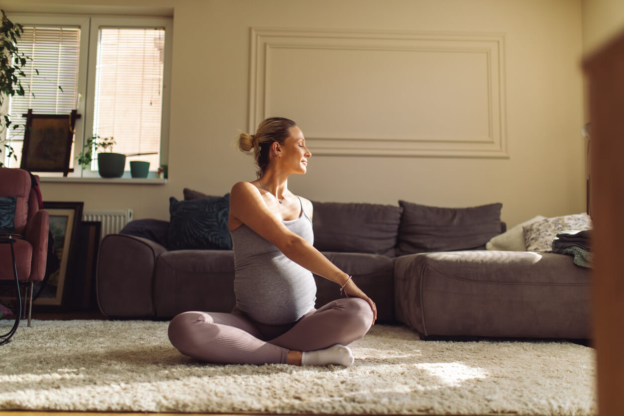 A pregnant woman does a yoga pose on the floor of a sunny room to improve her mental health.